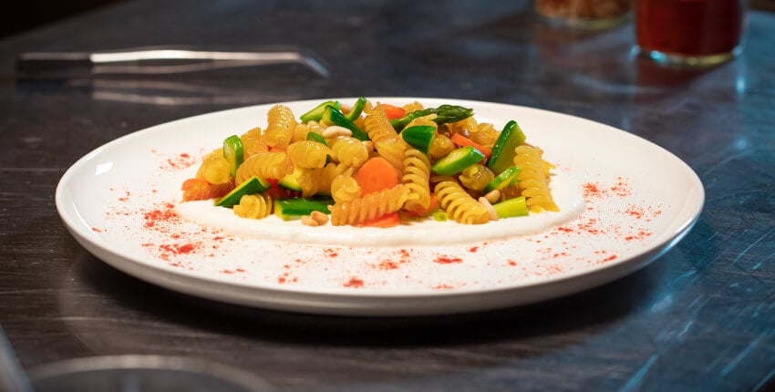 Piatto di fusilli arrostiti con verdure croccanti su crema di burrata